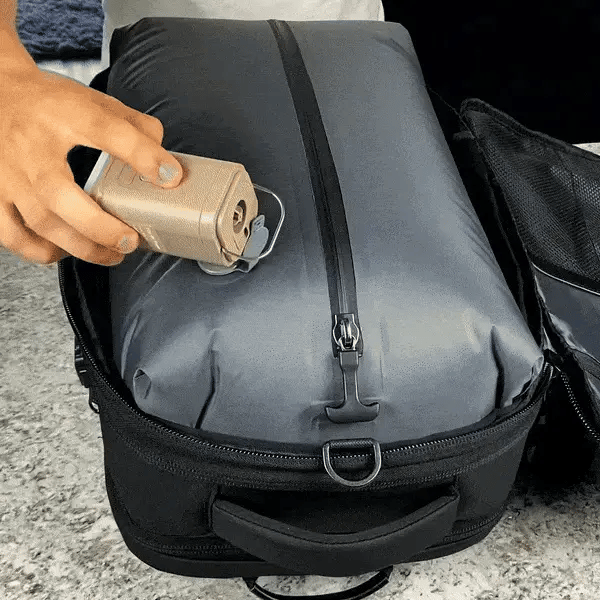 A hand using a vacuum sealer device on a black, vacuum-sealed travel bag.